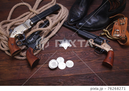 Old western revolver guns with sheriff badge and silver dollars with hat, rope and cowboy boots 76268271