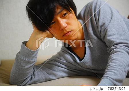 ベッドに横たわりテレビを見る男性 76274395