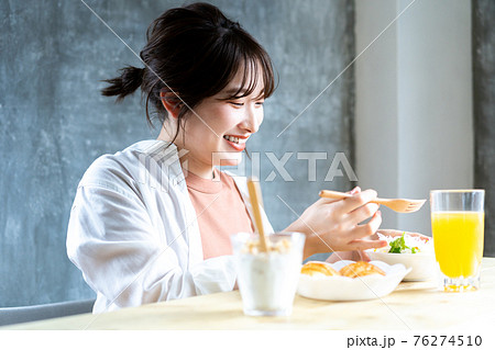朝日を浴びながら朝食を食べる若い女性 76274510