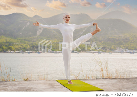 Kundalini yoga woman in white clothes and turban practices yoga kundalini on the background of the sea, mountains and sunset. Fighting face painting of the Indians shows her inner world. Visual 76275577