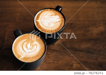 Two cappuccino coffee with latte art on wooden table. Black cups and beautiful milk foam. Soft focus 76276251