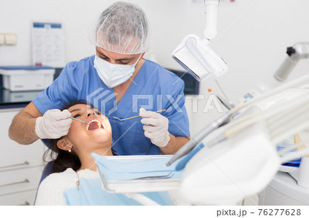Dentist man examining a latin female patient teeth Dentist man examining a latin female patient teeth 76277628
