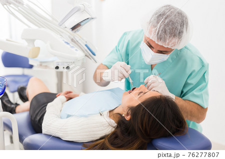 Dentist man examining a latin female patient teeth 76277807