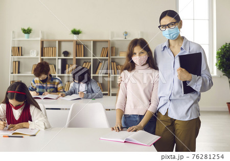 Portrait of female teacher and little schoolgirl in protective masks at school in class. Portrait of female teacher and little schoolgirl in protective masks at school in class. 76281254
