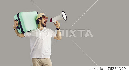 Tourist holding suitcase shouting in megaphone studio portrait over copy space 76281309