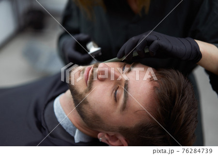 Young beautiful caucasian woman hairdresser cuts beard handsome man at modern barbershop Young beautiful caucasian woman hairdresser cuts beard handsome man at modern barbershop 76284739