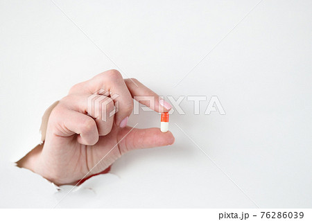 Female hand holds medical pill through hole through white paper 76286039