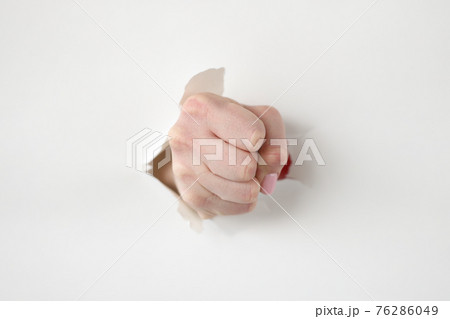 Tightly clenched fist through hole in white paper Tightly clenched fist through hole in white paper 76286049