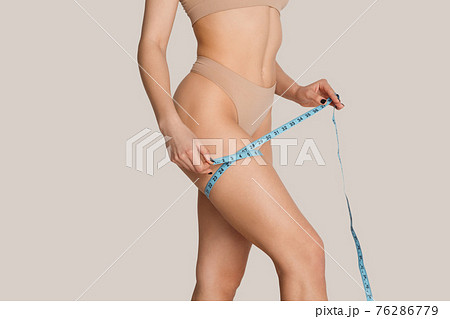 Beautiful female body in nude color underwear over grey background. Beautiful female body in nude color underwear over grey background. 76286779