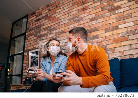 Shooting from below of happy young couple wearing medical protective masks playing video games on console 76288073