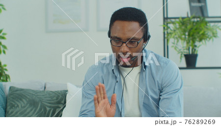 Serious focused afro american man wears headphones and head microphone uses laptop computer to make online video chat conference online during coronavirus. Serious focused afro american man wears headphones and head microphone uses laptop computer to make online video chat conference online during coronavirus. 76289269