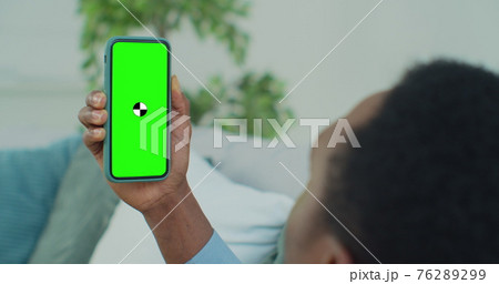 Back view of African man holding chroma key green screen smartphone watching content. African-American guy using mobile phone, browsing internet, watching content. Back view of African man holding chroma key green screen smartphone watching content. African-American guy using mobile phone, browsing internet, watching content. 76289299