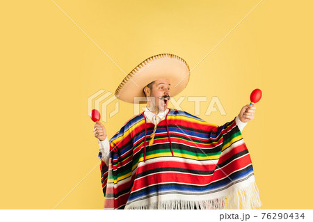 Happy man in sombrero and bright poncho isolated over yellow background 76290434