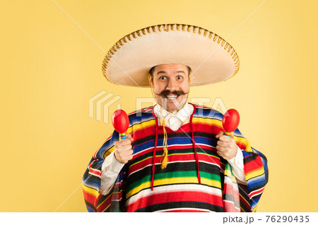 Happy man in sombrero and bright poncho isolated over yellow background 76290435