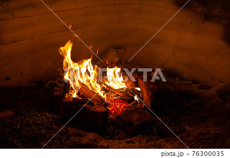 A campfire burns in the snow at night in the snow in the cold winter 76300035