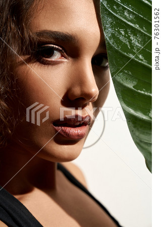 Woman hiding face behind big green leaf. Woman hiding face behind big green leaf. 76301562