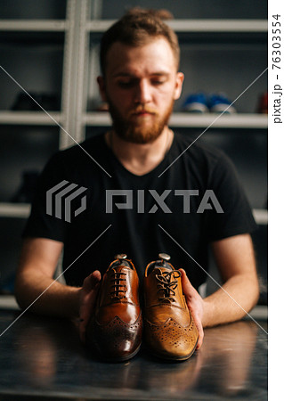 Portrait of male shoemaker holds old light brown leather shoe and repaired shiny shoes after restoration working. 76303554