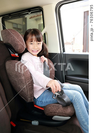 助手席に取り付けたジュニアシートでシートベルトを着用する女の子の写真素材