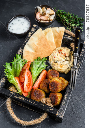 Traditional homemade Hummus chickpea, falafel, pita bread and fresh vegetables. Black background. Top view Traditional homemade Hummus chickpea, falafel, pita bread and fresh vegetables. Black background. Top view 76307637