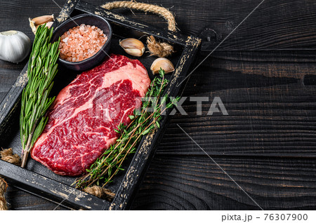 Raw prime rib eye beef meat steak in a butcher wooden tray with herbs. Black wooden background. Top view. Copy space Raw prime rib eye beef meat steak in a butcher wooden tray with herbs. Black wooden background. Top view. Copy space 76307900