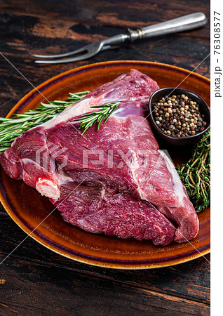 Raw lamb mutton thigh or leg with rosemary and thyme in rustic plate. Dark wooden background. Top view 76308577