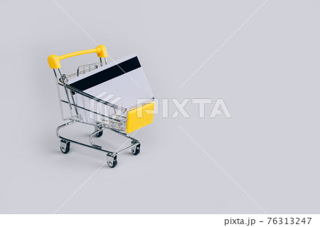 Yellow shopping cart with credit card inside on light gray background with copy space for text. Sale event, Black Friday and Cyber Monday concept in colors of the year 2021. Selective focus 76313247