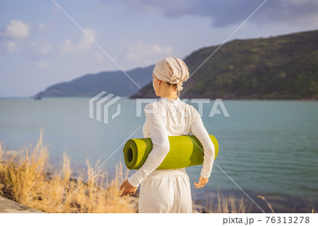 Kundalini yoga woman in white clothes and turban practices yoga kundalini on the background of the sea, mountains and sunset. Fighting face painting of the Indians shows her inner world. Visual Kundalini yoga woman in white clothes and turban practices yoga kundalini on the background of the sea, mountains and sunset. Fighting face painting of the Indians shows her inner world. Visual 76313278