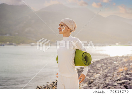 Kundalini yoga woman in white clothes and turban practices yoga kundalini on the background of the sea, mountains and sunset. Fighting face painting of the Indians shows her inner world. Visual 76313279