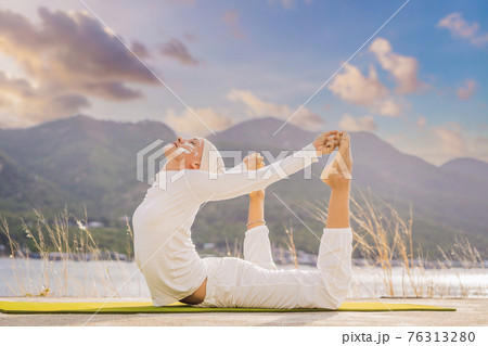 Kundalini yoga woman in white clothes and turban practices yoga kundalini on the background of the sea, mountains and sunset. Fighting face painting of the Indians shows her inner world. Visual Kundalini yoga woman in white clothes and turban practices yoga kundalini on the background of the sea, mountains and sunset. Fighting face painting of the Indians shows her inner world. Visual 76313280