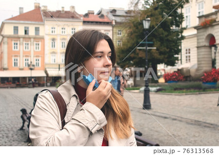 Beautiful young woman, taking off her disposable protective face mask walking the street. Pandemic prevention, air pollution, seasonal epidemic and lockdown end concept. After quarantine life Beautiful young woman, taking off her disposable protective face mask walking the street. Pandemic prevention, air pollution, seasonal epidemic and lockdown end concept. After quarantine life 76313568