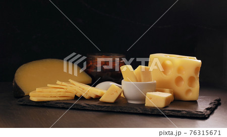Several types of yellow cheese on black stone board. 76315671