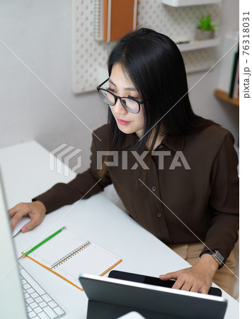 Female office worker concentrating on her work with computer and office supplies Female office worker concentrating on her work with computer and office supplies 76318031