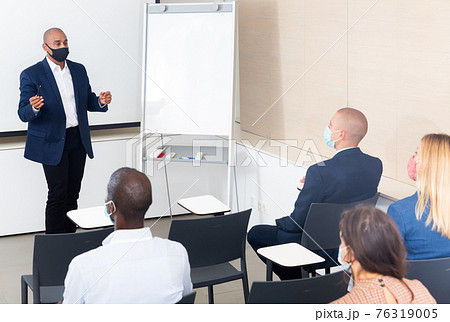 Man in protective mask giving presentation to colleagues at international meeting Man in protective mask giving presentation to colleagues at international meeting 76319005
