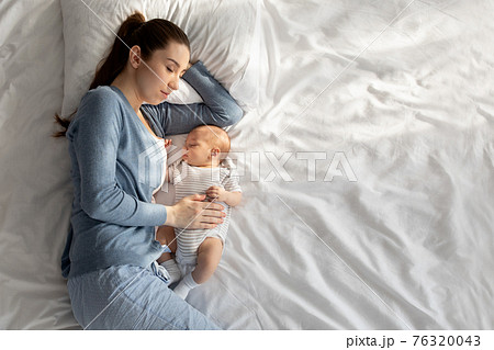 Co-sleeping with baby. Young woman napping in bed with her newborn child Co-sleeping with baby. Young woman napping in bed with her newborn child 76320043