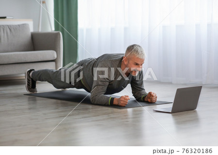 Athletic mature bearded man doing exercises at home, using laptop Athletic mature bearded man doing exercises at home, using laptop 76320186