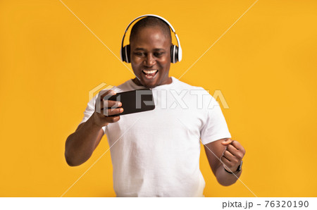 Excited happy middle aged african american male in white t-shirt and headphones expresses success 76320190