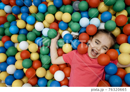 a child in the children's playroom. The girl is having fun among the colorful balls. Dry Pool Party 76320665