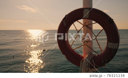 Lifebuoy hanging on the background of the sea at sunrise. Morning at the sea Lifebuoy hanging on the background of the sea at sunrise. Morning at the sea 76321136