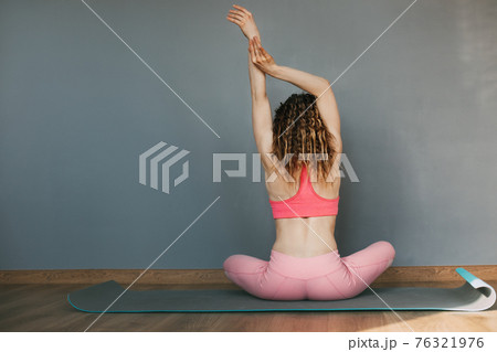 A girl with curly hair sits in a lotus position on a yoga mat and meditates after a workout. Rear view, space for text A girl with curly hair sits in a lotus position on a yoga mat and meditates after a workout. Rear view, space for text 76321976