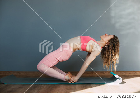 A young woman in sportswear practices yoga and performs asanas in a yoga class or at home. Yoga, sports, fitness. The concept of mental health and healthy lifestyle 76321977
