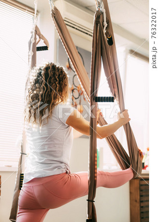 A girl with curly hair practices yoga with a hammock. Yoga, aero yoga, fitness, lifestyle. Rear view 76322017