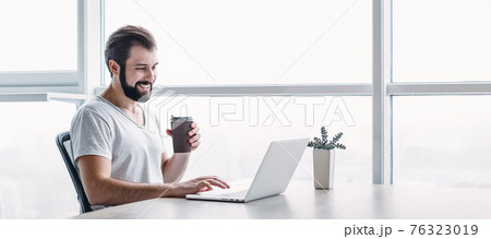 Website header of Portrait of smiling man sitting in the office with laptop and coffee. Side view Website header of Portrait of smiling man sitting in the office with laptop and coffee. Side view 76323019