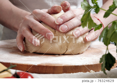Women's hands knead the dough from wheat flour 76324629