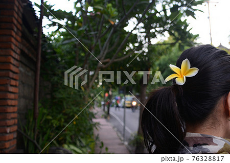 インドネシアバリ島ウブドの路上 プルメリアの花を髪に飾った黒髪ポニーテールの日本人女性観光客の後ろ姿の写真素材