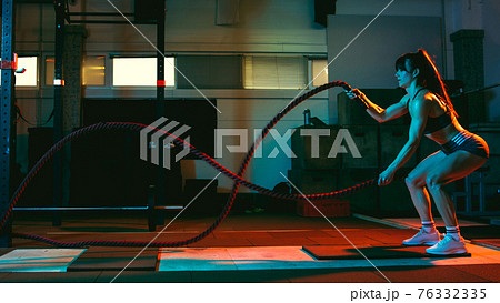 Young athletic woman, fitness instructor training in gym in mixed neon light. 76332335