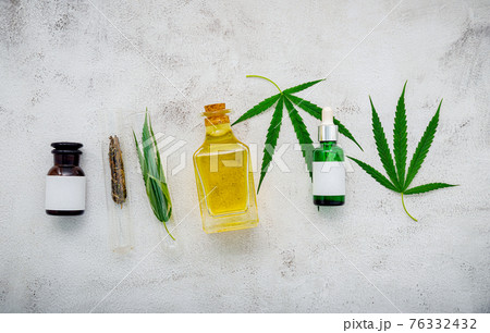 Glass bottle of cannabis oil and hemp leaves set up on concrete background. Glass bottle of cannabis oil and hemp leaves set up on concrete background. 76332432