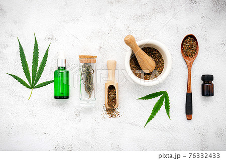 Glass bottle of cannabis oil with white mortar and hemp leaves set up on concrete background. Glass bottle of cannabis oil with white mortar and hemp leaves set up on concrete background. 76332433