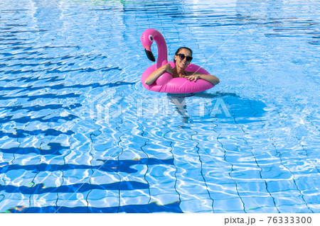 Young women pool. Happy young sexy girl in bikini swimsuit, sunglasses with pink inflatable flamingo float in blue water. Travel holidays vacation. Beauty, wellness, lifestyle. Young women pool. Happy young sexy girl in bikini swimsuit, sunglasses with pink inflatable flamingo float in blue water. Travel holidays vacation. Beauty, wellness, lifestyle. 76333300