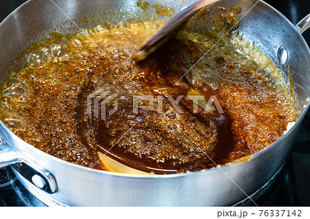 cooking salted butter caramel sauce at home kitchen - mixing boiled mixture of sugar and butter with wooden culinary spatula in steel pan close up cooking salted butter caramel sauce at home kitchen - mixing boiled mixture of sugar and butter with wooden culinary spatula in steel pan close up 76337142