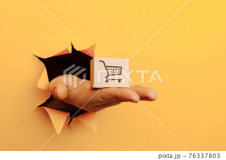 Hand with a box through a yellow paper hole. Delivery concept Hand with a box through a yellow paper hole. Delivery concept 76337803